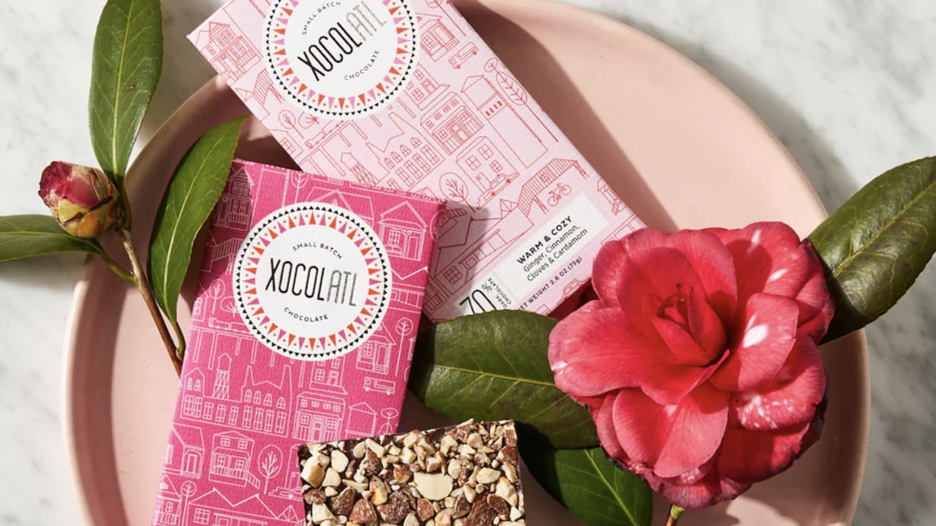 Two pink chocolate bars with house patterns, a red camellia flower, and green leaves on a marble surface in Atlanta, Georgia.